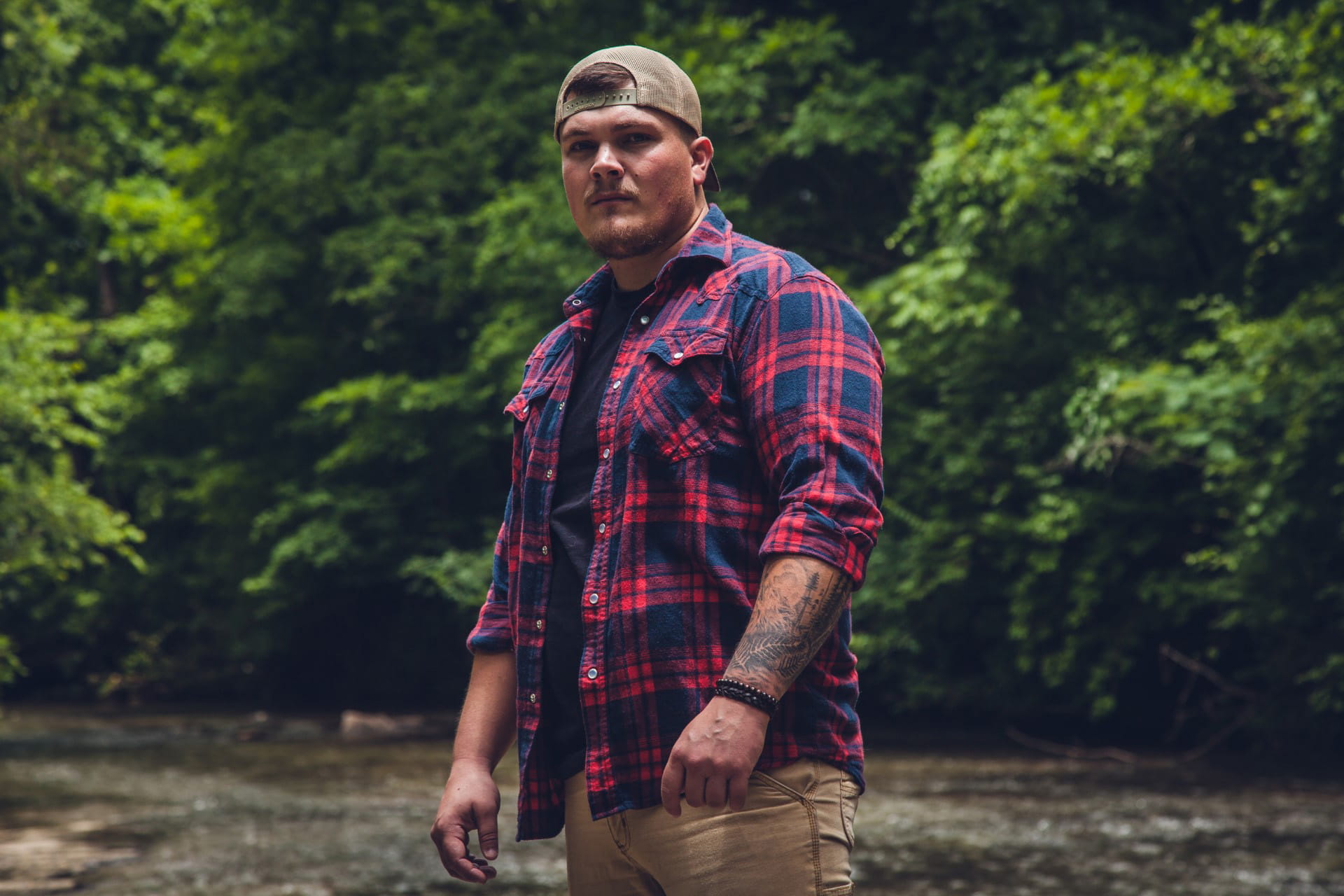 Shawn David in red and blue flannel shirt and khakis, standing in front of trees.