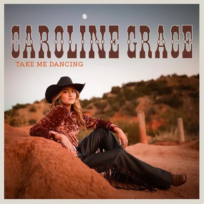 Album cover of Caroline Grace's "Take Me Dancing" - Caroline in cowboy hat, chaps, and cowboy boots, seated on a country road with long hair down.